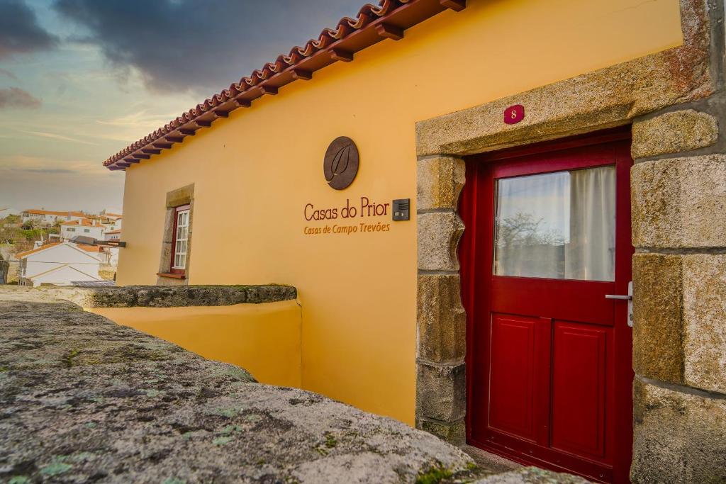 a red door on the side of a yellow building at Casas do Prior in Trevões