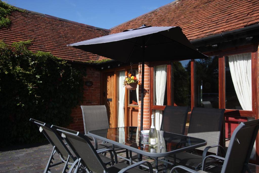 a glass table with an umbrella on a patio at Whitley Elm Cottages in Warwick