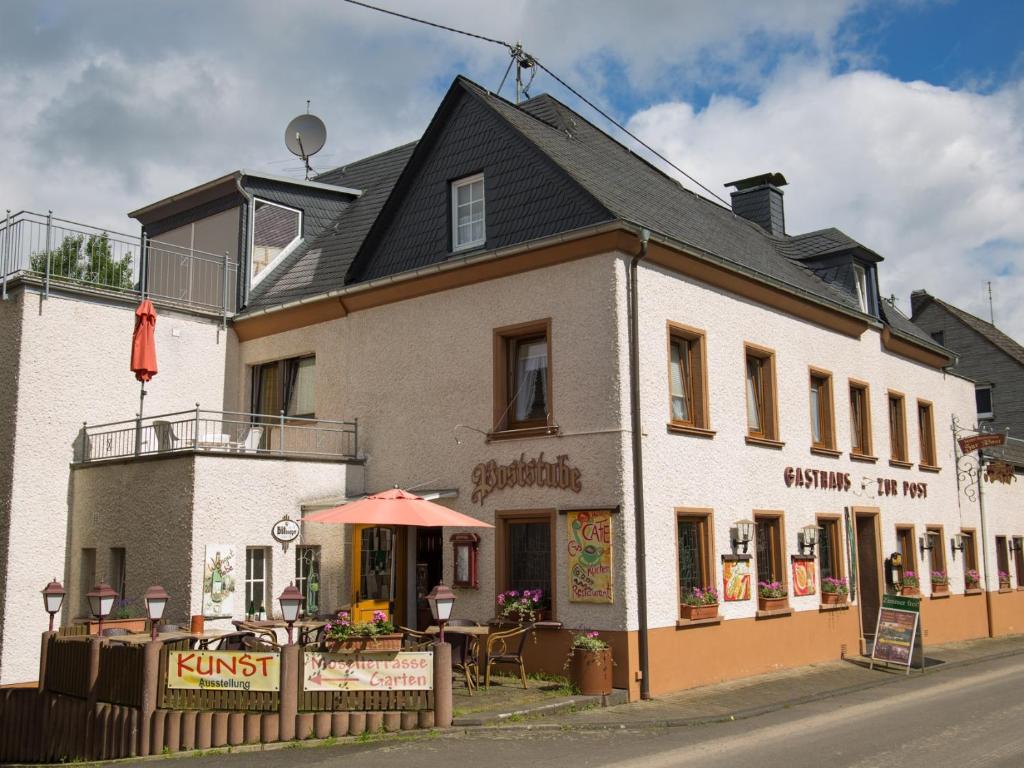 a large white building with an umbrella on a street at Hotel zur Post - Burg an der Mosel in Burg (an der Mosel)