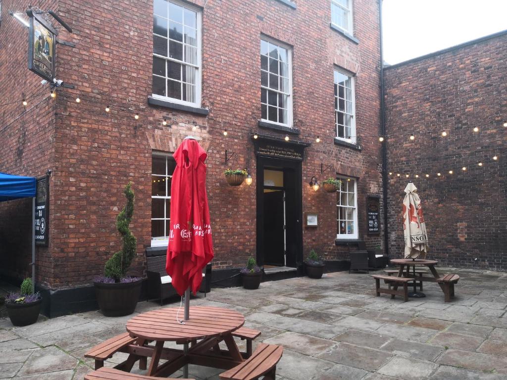 um pátio com mesas e um guarda-chuva vermelho em frente a um edifício de tijolos em The Commercial Bar & Hotel em Chester