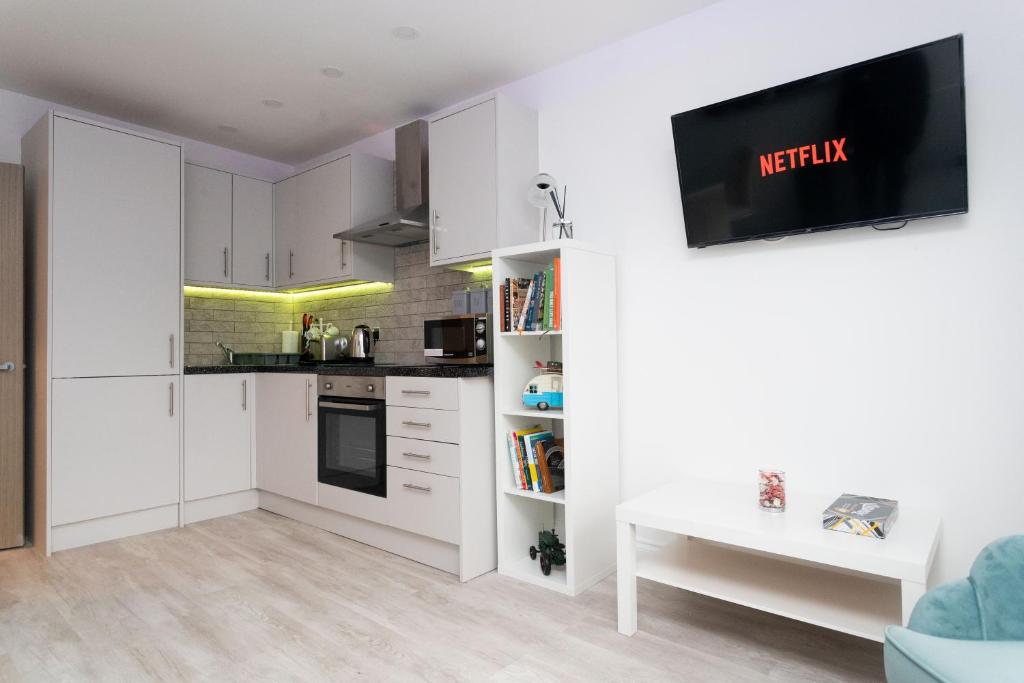 uma cozinha com armários brancos e uma televisão na parede em The Avenue Apartments em Leeds