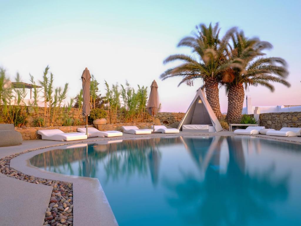 uma piscina num resort com palmeiras e guarda-sóis em Ostraco Suites em Míconos