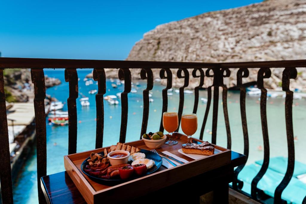 een dienblad met eten en drinken op een tafel naast het water bij Hotel San Andrea in Xlendi