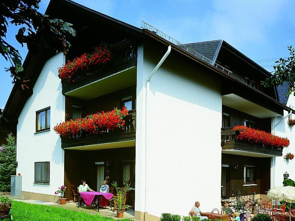 a white building with red flowers on the balconies at Pension Waldesruh in Welschneudorf