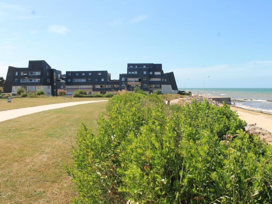 a bush in front of a beach with buildings at Duplex Croisette Juno Beach in Bernières-sur-Mer