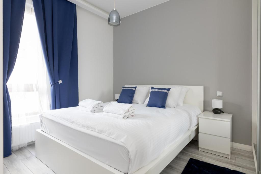 ein weißes Bett mit blauen Kissen im Schlafzimmer in der Unterkunft Wilanów Gardens with Balcony in Warschau