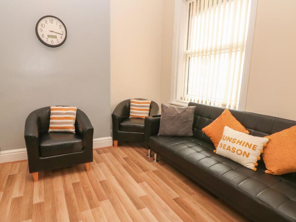 a living room with a black leather couch and two chairs at North Shore Apartment in Blackpool