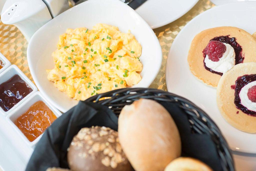A breakfast spread includes scrambled eggs, breads, pastries, fruit preserves and pancakes.