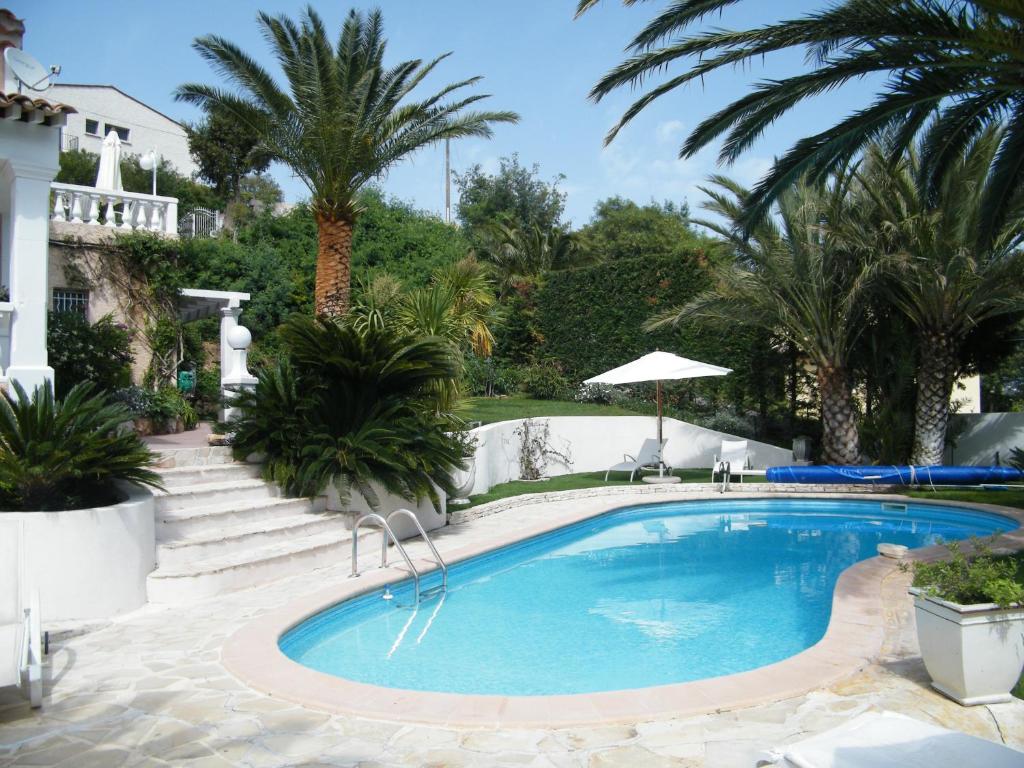 a swimming pool with palm trees and a house at L'oasis-LES ISSAMBRES in Les Issambres