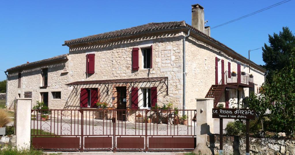 ein altes Steinhaus mit roten Rollläden und einem Tor in der Unterkunft LE RELAIS D'ARZAC in Cahuzac-sur-Vère