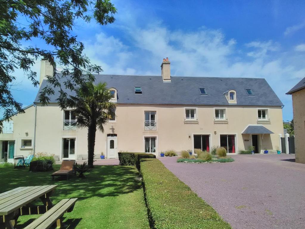 una gran casa blanca con una mesa de picnic delante de ella en La Maison Periot, en Trévières