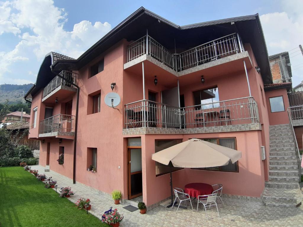 um edifício cor-de-rosa com uma mesa e um guarda-chuva em Къща за гости Романс em Yagodina