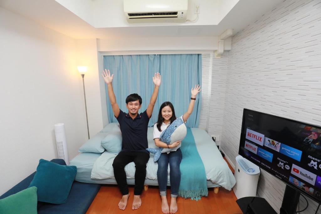 a man and woman sitting on a bed with their hands in the air at IBASHO ShibuyaDogenzaka810 in Tokyo