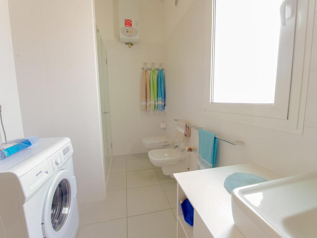 a white bathroom with a washing machine and a toilet at Portofelice Camping Village in Eraclea Mare