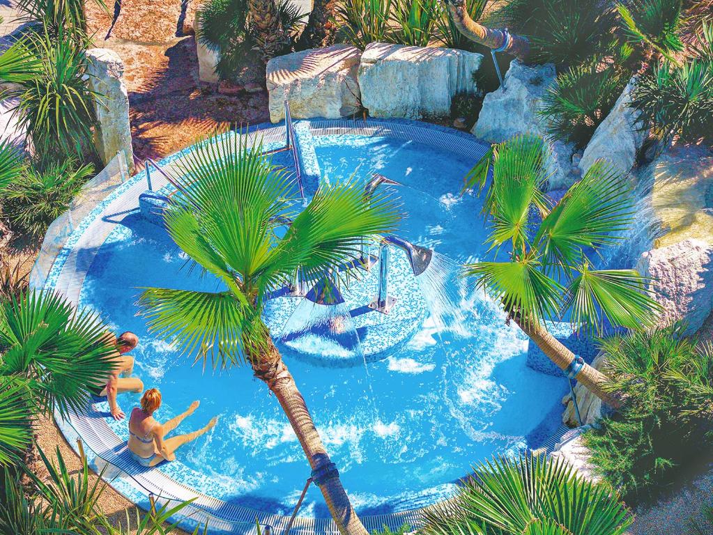 a group of people in a large swimming pool with palm trees at Portofelice Camping Village in Eraclea Mare