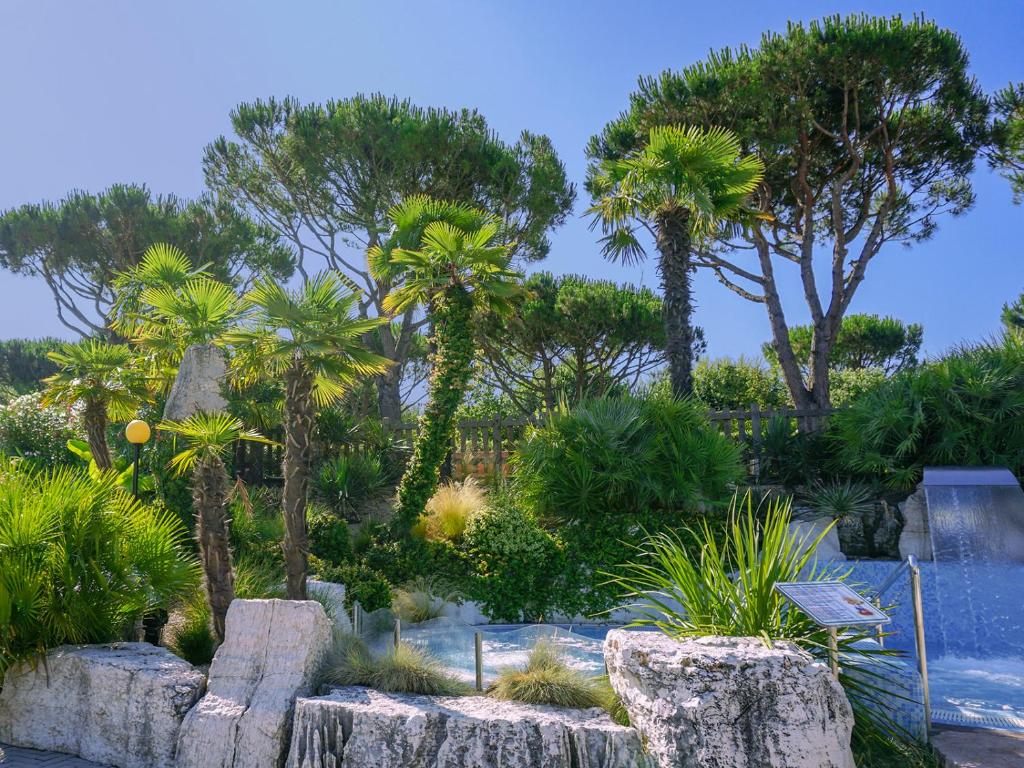 a garden with trees and rocks and palm trees at Portofelice Camping Village in Eraclea Mare