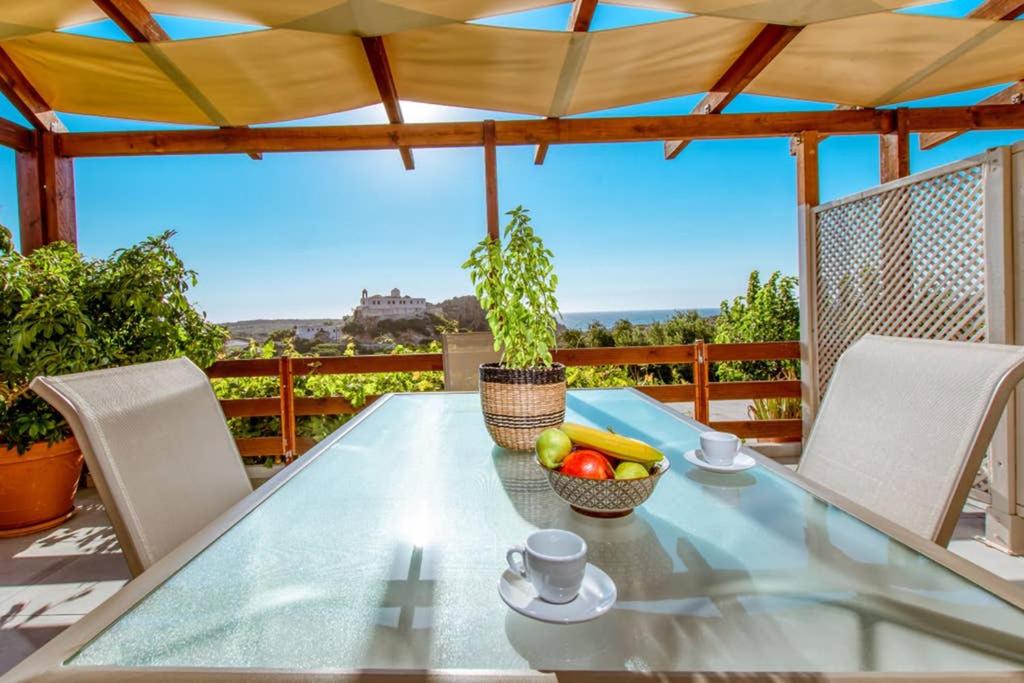 a glass table with a bowl of fruit on a patio at Iliovasilema Apartments in Elafonisi