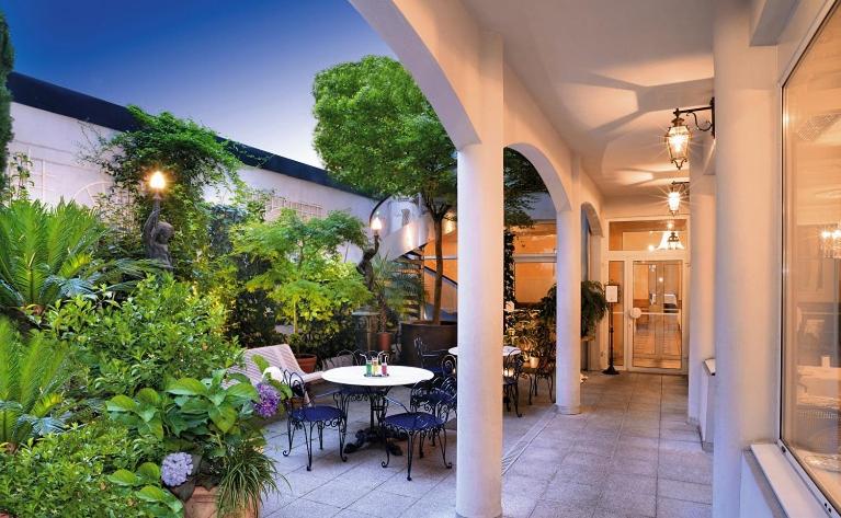 an outdoor patio with a table and chairs and plants at Hôtel Gloria & Avenue in Lourdes