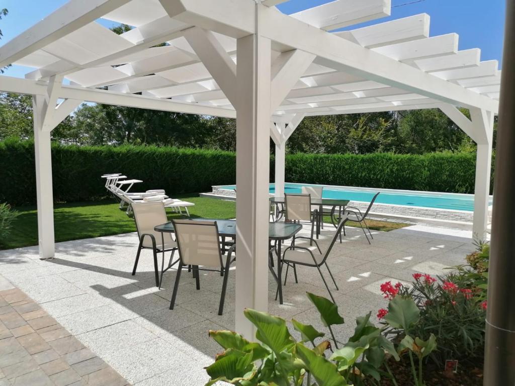 een witte pergola met tafels en stoelen naast een zwembad bij Dimora al Bosco in Cessalto