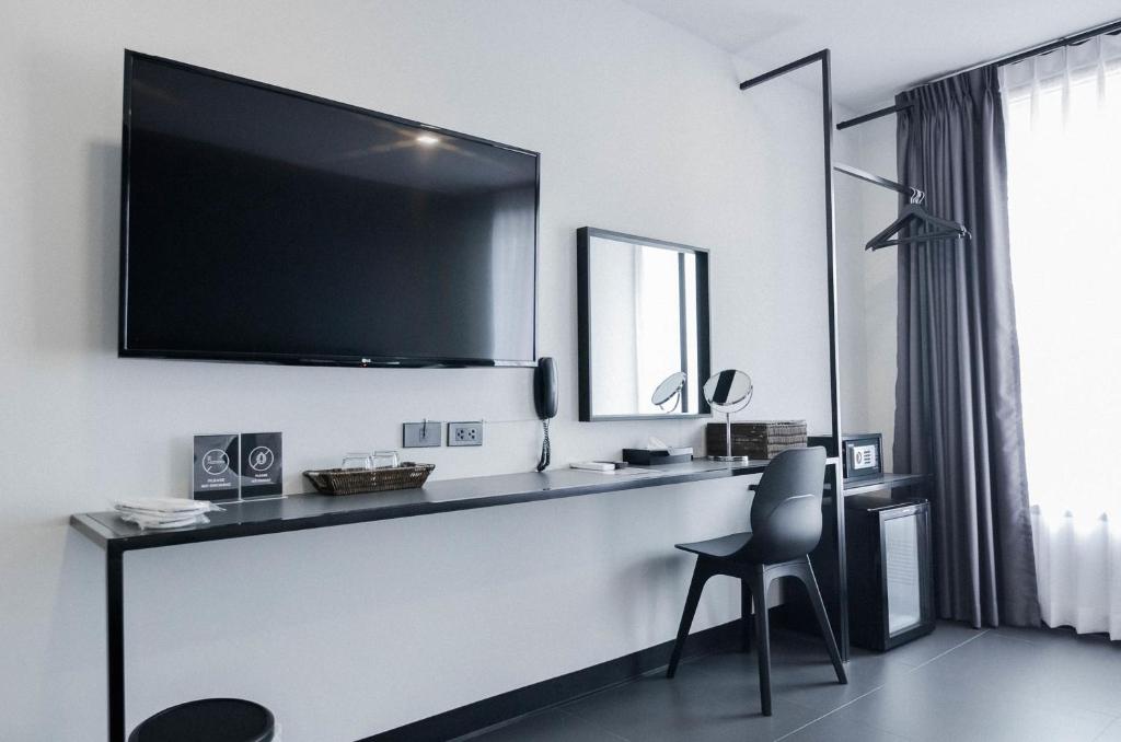 A room-side work desk runs beneath a wall-mounted television beside a chair and mini-fridge.