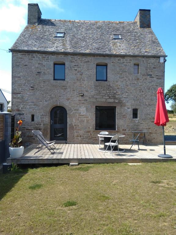 un bâtiment avec une terrasse, une table et un parapluie rouge dans l'établissement Les charmantes pierres percées, à Ploumilliau