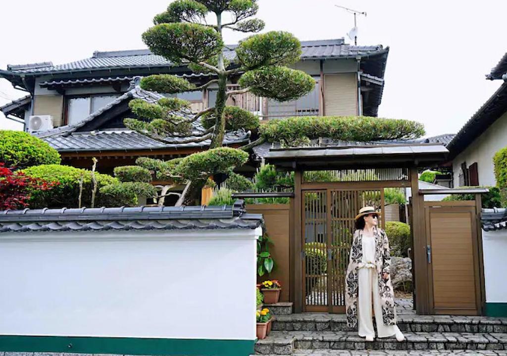 Eine Frau steht auf einer Treppe vor einem Haus. in der Unterkunft 太宰苑 - Dazaien Traditional Japanese houses in Dazaifu