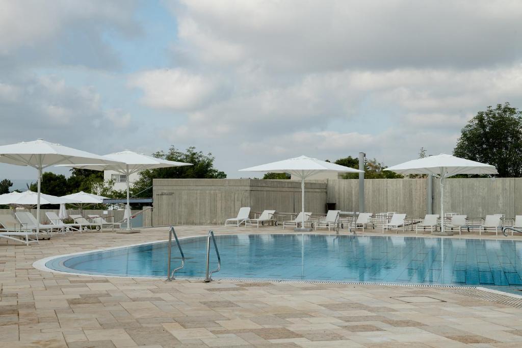 a swimming pool with white chairs and umbrellas at Elma Hotel and Art Complex in Zikhron Ya'akov