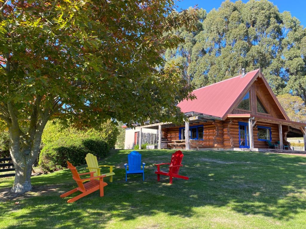a group of chairs sitting in the grass in front of a log cabin at Tree Hut Cottage in Masterton