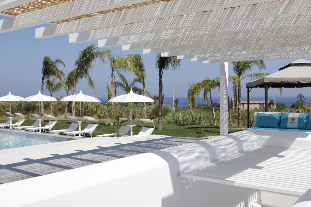a swimming pool with white chairs and umbrellas at Il Borghetto Resort & Spa in Tropea