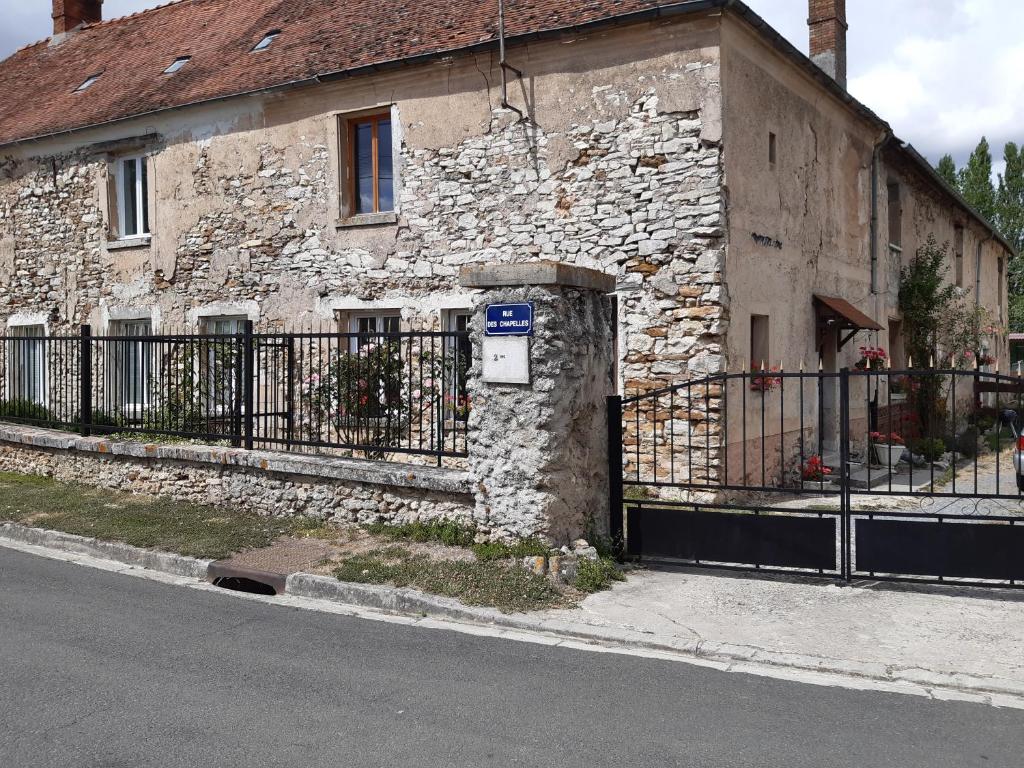 un antiguo edificio de piedra con una valla al lado de una calle en Ferme Des Chapelles, en Fresnes-en-Tardenois