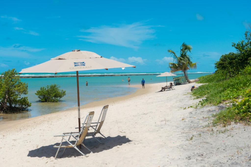 een strand met 2 stoelen en een parasol bij Polinésia Resort Beira Mar Muro Alto Porto de Galinhas in Porto De Galinhas