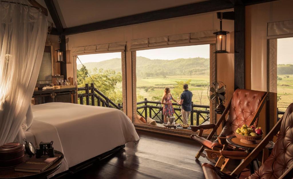 a bedroom with a bed and two people looking out the window at Four Seasons Tented Camp Golden Triangle in Golden Triangle