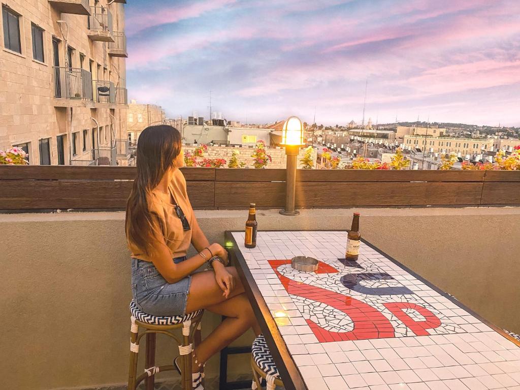 a woman sitting at a table on a balcony at The Post Hostel Jerusalem in Jerusalem