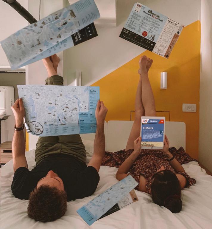 two people laying on a bed reading newspapers at The Post Hostel Jerusalem in Jerusalem