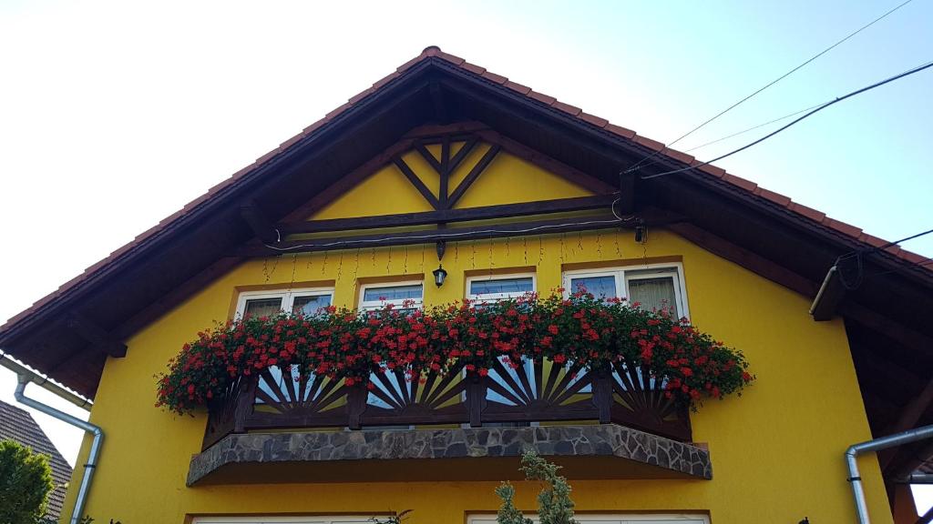 a yellow house with a balcony with red flowers at Hazanéző Panzió in Corund