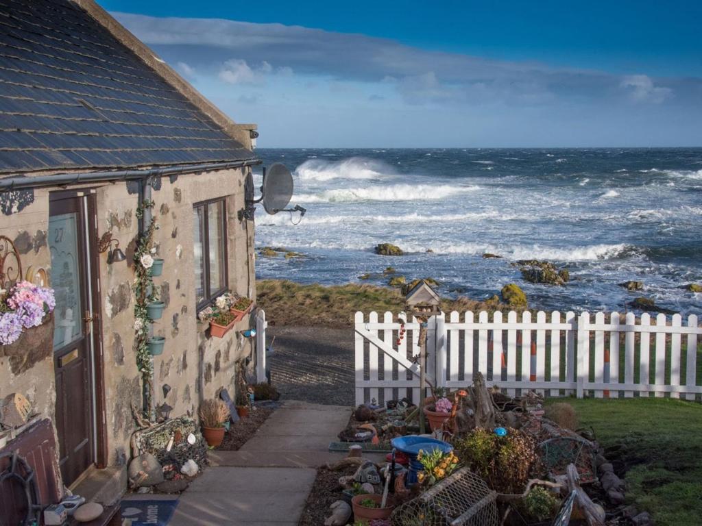 a house with a fence next to the ocean at Pew with a View - Seafront Cottages in Sandhaven