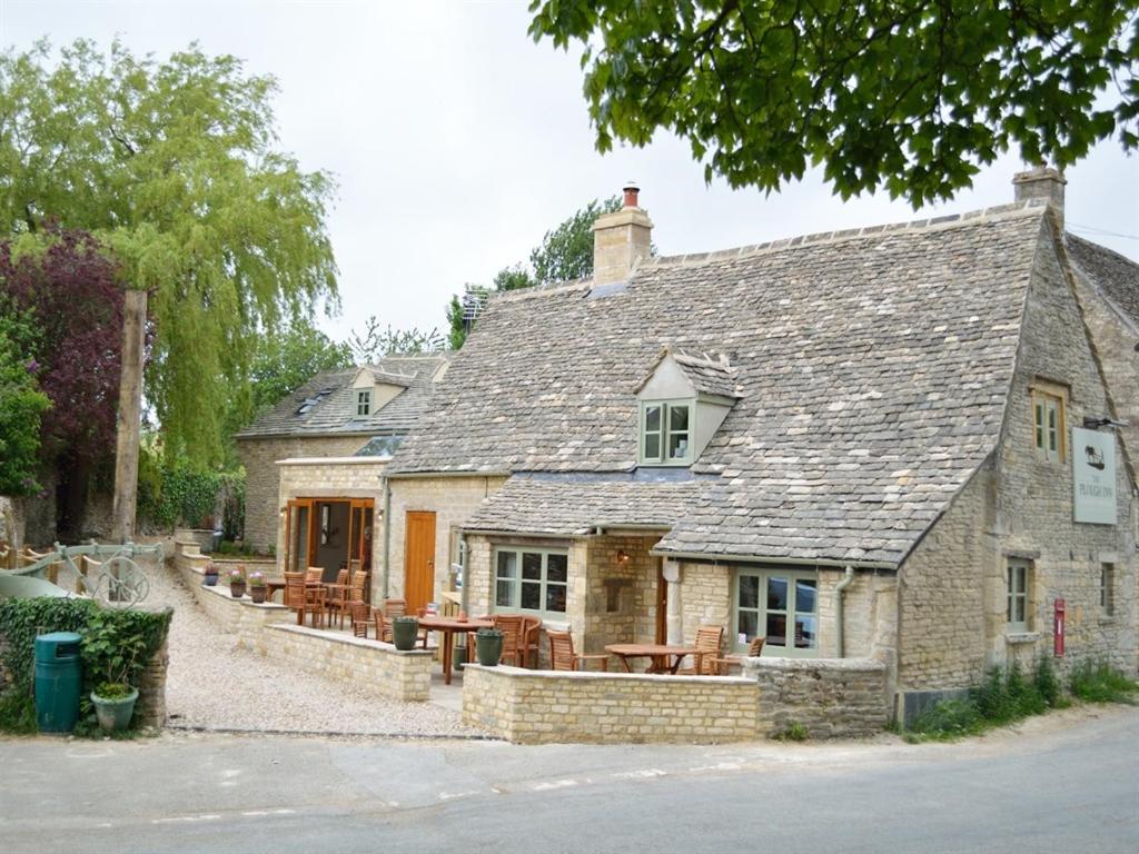 uma antiga casa de pedra com uma mesa e cadeiras em The Plough Inn em Cheltenham