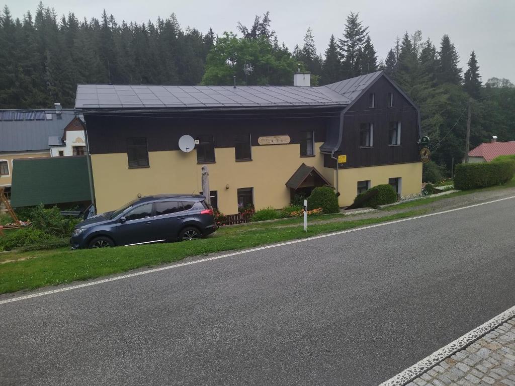 una casa negra y amarilla con un coche aparcado a un lado de la carretera en Penzion Borovice, en Josefŭv Dŭl