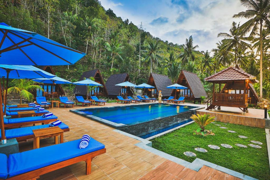 a pool at a resort with blue chairs and umbrellas at Mahaloka Valley Nusa Penida in Nusa Penida