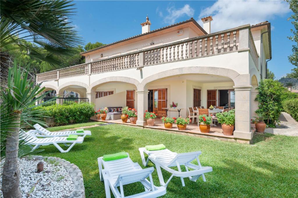a villa with a patio and lawn with white chairs at Chilllife in Port d'Alcudia
