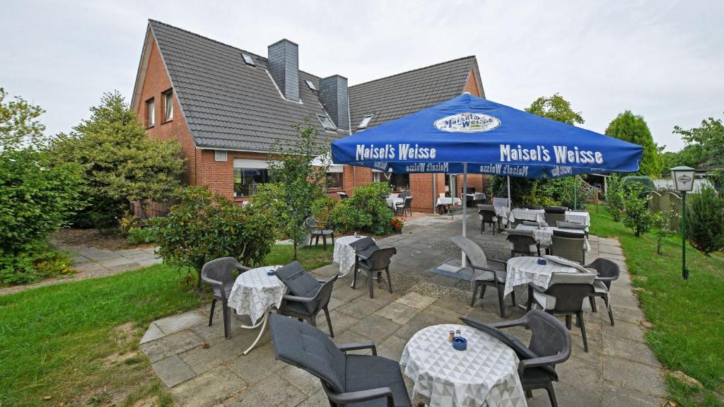 un restaurante con mesas y sillas bajo una sombrilla azul en Hotel vom Land zum Meer en Jork