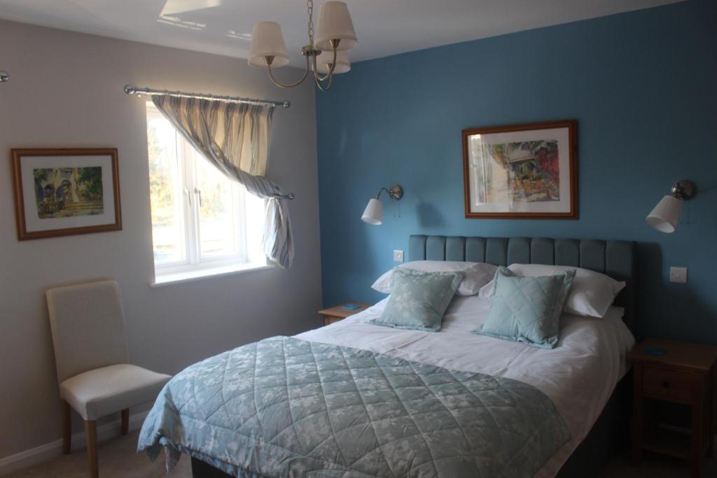 a bedroom with a bed with blue walls and a window at The Swallows in Seend
