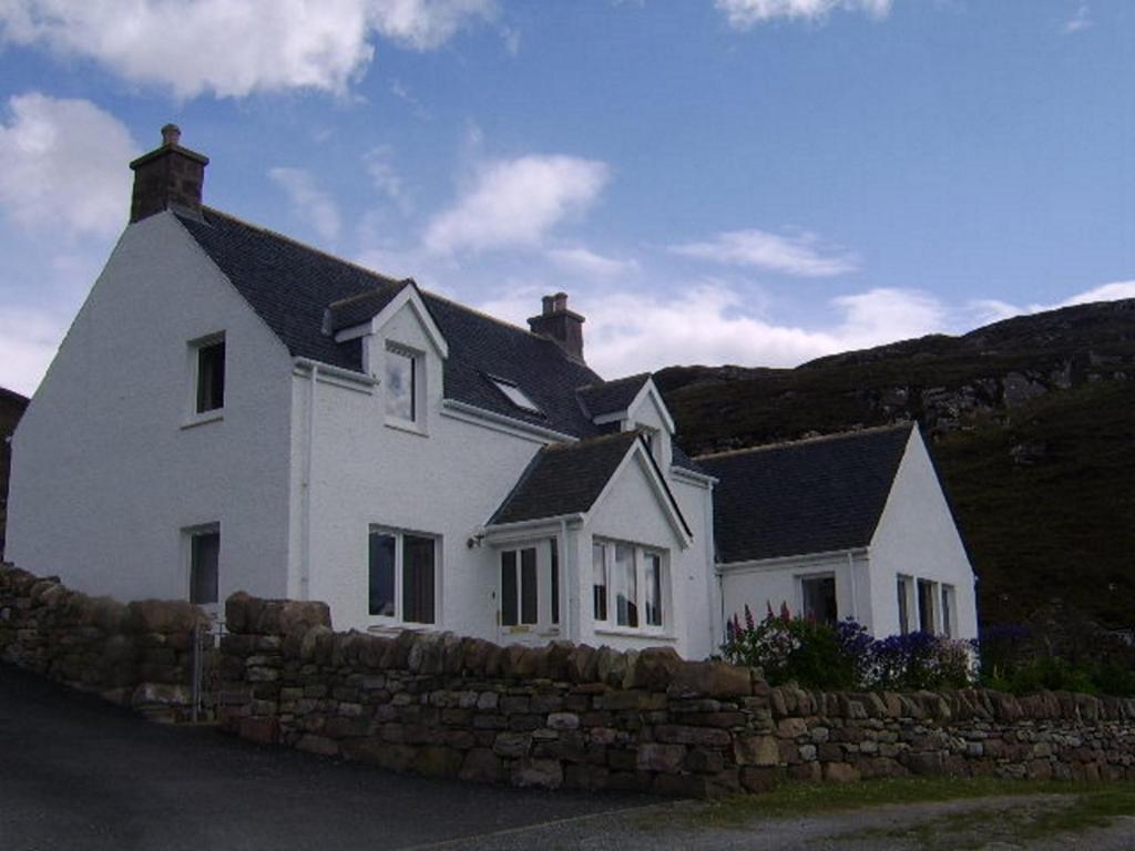 uma casa branca com uma cerca de pedra à frente. em Top House em Ullapool