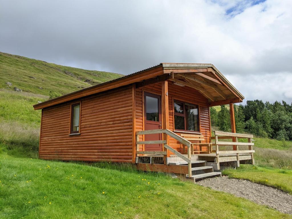 a wooden cabin on a hill with a grassy field at St&oacute;ra-Vatnshorn in B&uacute;&eth;ardalur