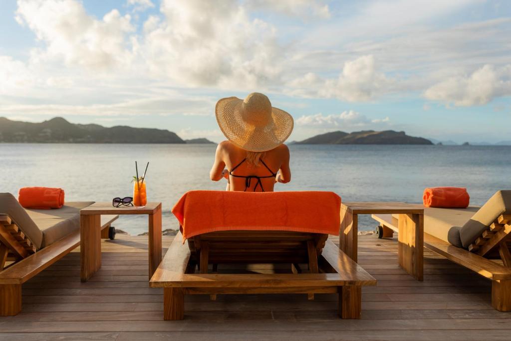 a person wearing a hat sitting on a chair looking at the ocean at Hotel Christopher Saint Barth in Gustavia