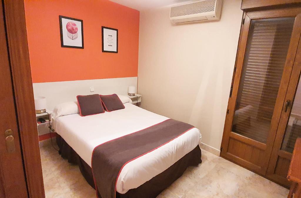 1 dormitorio pequeño con 1 cama y pared de color naranja en Hospedaje Bar El Gato del Acueducto, en Segovia