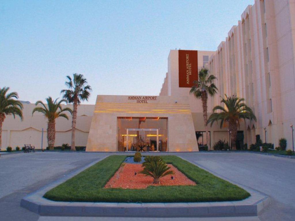 a hotel with palm trees in front of a building at Amman Airport Hotel in Al Qasţal