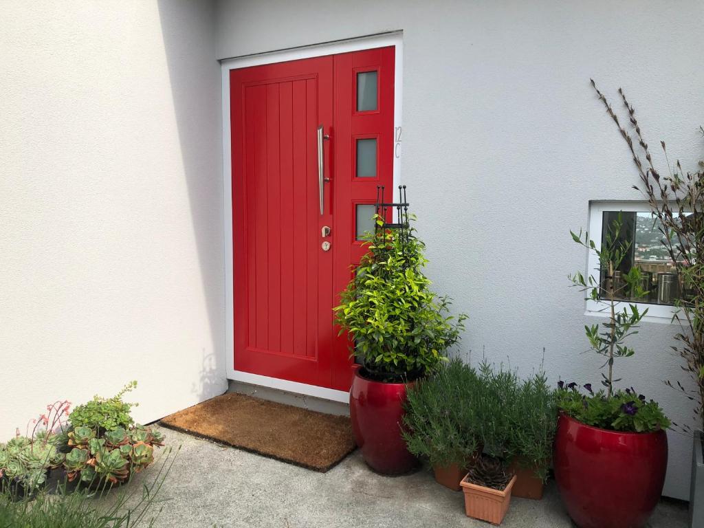 uma porta vermelha com vasos de plantas em frente a uma casa em Executive style bedroom em Kelburn