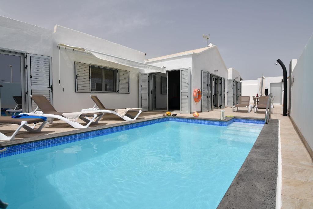 a swimming pool with chairs and a house at Villa Malagueñas in Puerto del Carmen