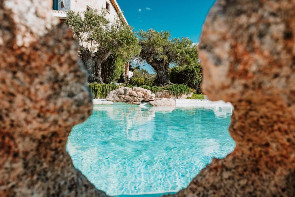 a view of a swimming pool through a rock at Hotel Pulicinu in Baja Sardinia
